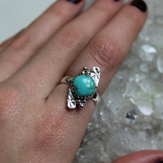 A sterling silver ring with a turquoise gemstone and flower design displayed on a hand