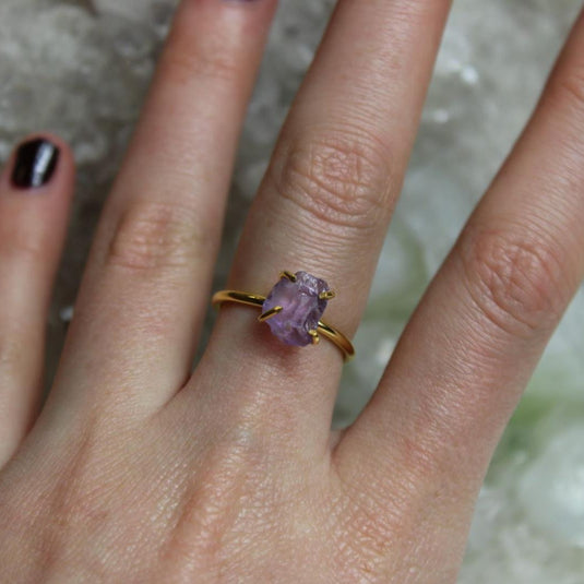 A hand wearing a Raw Amethyst Ring with a gold vermeil prong setting