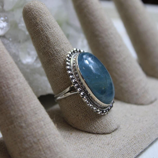 A large oval Aquamarine ring displayed on a ring holder, with other ring holders visible in the background.