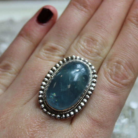 A large oval Aquamarine gemstone set in a silver ring with a beaded border. 