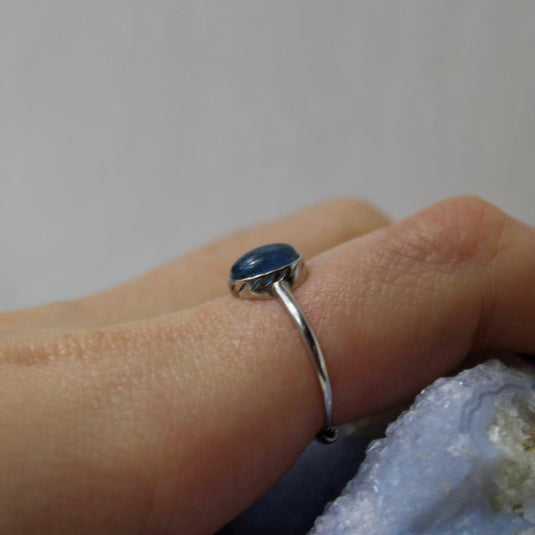 An oval-shaped aquamarine gemstone set in a sterling silver ring, shown on a hand against a blue background.