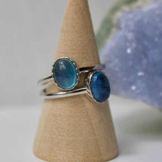 An oval-shaped aquamarine gemstone set in a sterling silver ring, shown on a jewellery stand against a blue background.