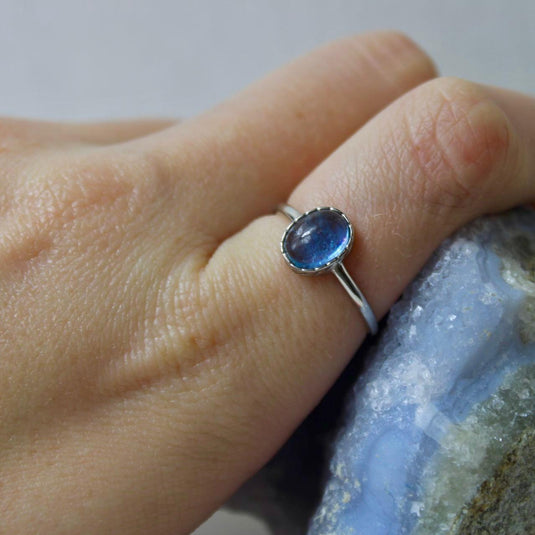 An oval-shaped aquamarine gemstone set in a sterling silver ring, shown on a hand against a blue background.