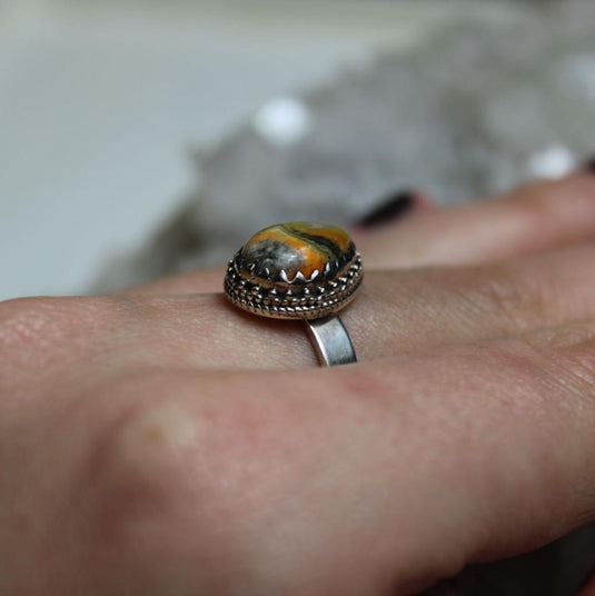 A touch of nature's beauty: Bumblebee Jasper ring shimmers on a hand surrounded by crystals.

