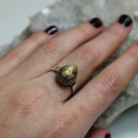 A touch of nature's beauty: Bumblebee Jasper ring shimmers on a hand surrounded by crystals.

