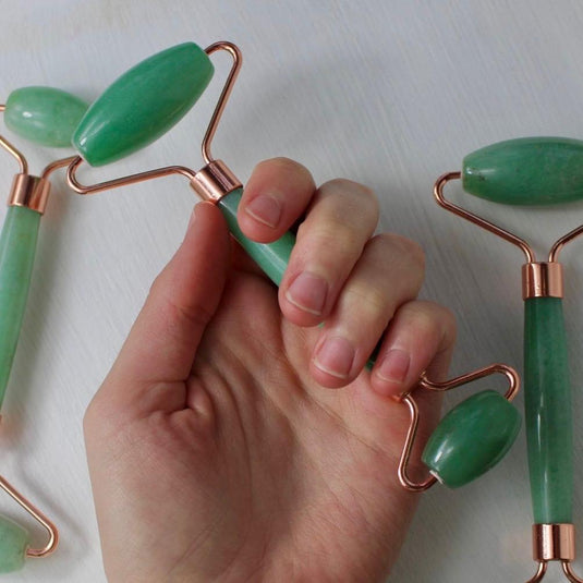 A person's hand holding a green aventurine massage roller with a rose gold handle.