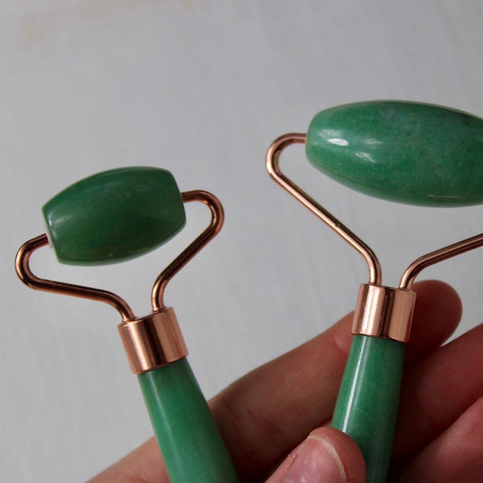 A person's hand holding a green aventurine massage roller with a rose gold handle.