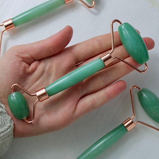 A person's hand holding a green aventurine massage roller with a rose gold handle.