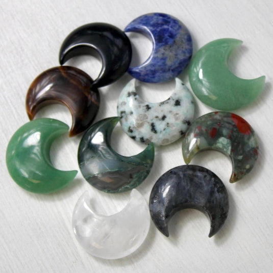 A collection of crescent moon-shaped crystal gemstones in various colours, including green, blue, brown, black, and clear quartz