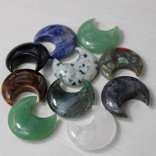 A collection of crescent moon-shaped crystal gemstones in various colours, including green, blue, brown, black, and clear quartz