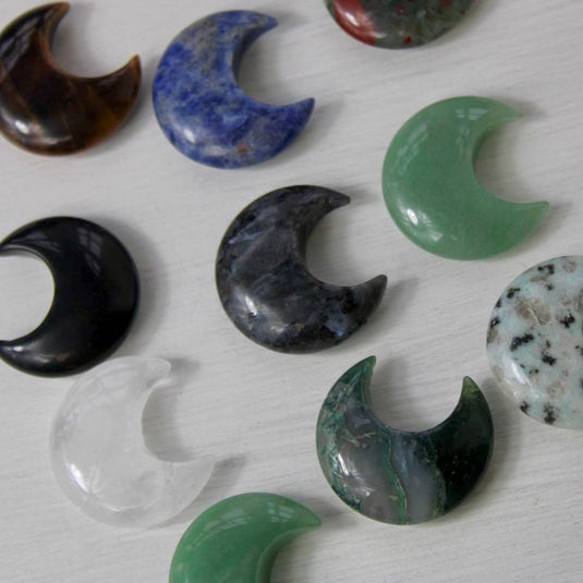 A collection of crescent moon-shaped crystal gemstones in various colours, including green, blue, brown, black, and clear quartz