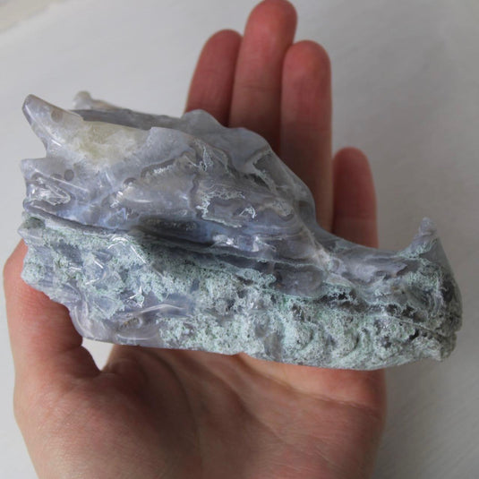 A hand-carved moss agate dragon head, showing intricate details like horns, teeth, and scales. The stone has a beautiful blend of blue, purple, and green hues.