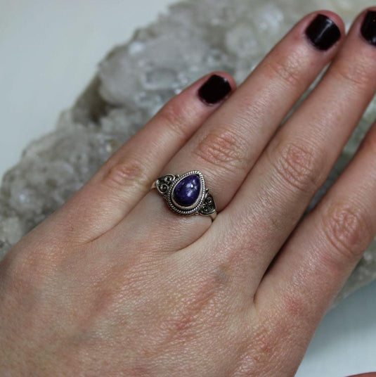 A stunning tear drop-shaped charoite gemstone set in a silver band.