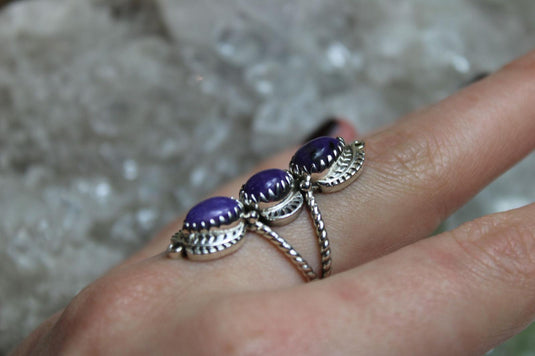 A stunning charoite ring featuring three vibrant purple gemstones with swirling patterns, set in a delicate silver band.