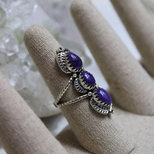 A stunning charoite ring featuring three vibrant purple gemstones with swirling patterns, set in a delicate silver band.