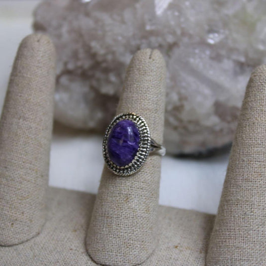 A large oval Charoite gemstone set in a sterling silver ring with a beaded border, displayed on a ring sizer.