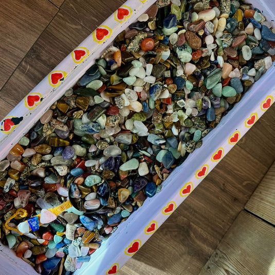 A container filled with crystal confetti, featuring a variety of colourful tumbled stones.