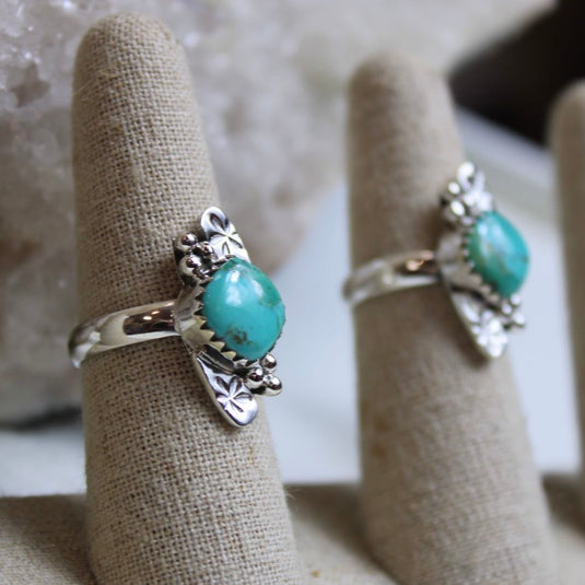 A side angle of two sterling silver rings with turquoise gemstones and flower designs, displayed on ring stands