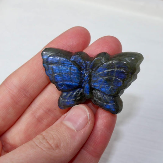 A hand holding a blue and black labradorite butterfly carving, showcasing the stone's iridescent properties.