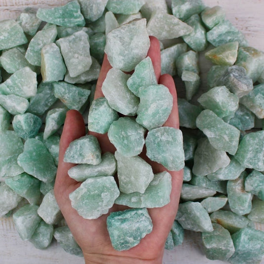 A hand holding a pile of raw green Aventurine stones.