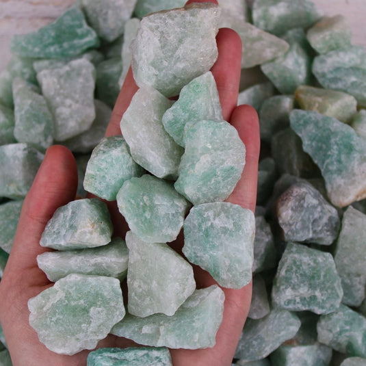 A hand cupping a handful of raw green Aventurine stones.