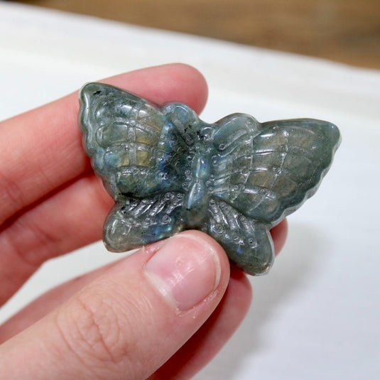 A hand holding a blue and green labradorite butterfly carving, showcasing the stone's iridescent properties.