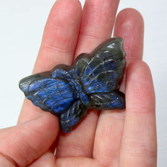 A hand holding a blue and black labradorite butterfly carving, showcasing the stone's iridescent properties.