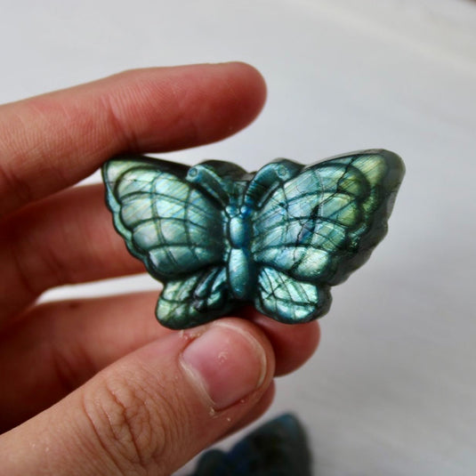 A hand holding a blue and green labradorite butterfly carving, showcasing the stone's iridescent properties.