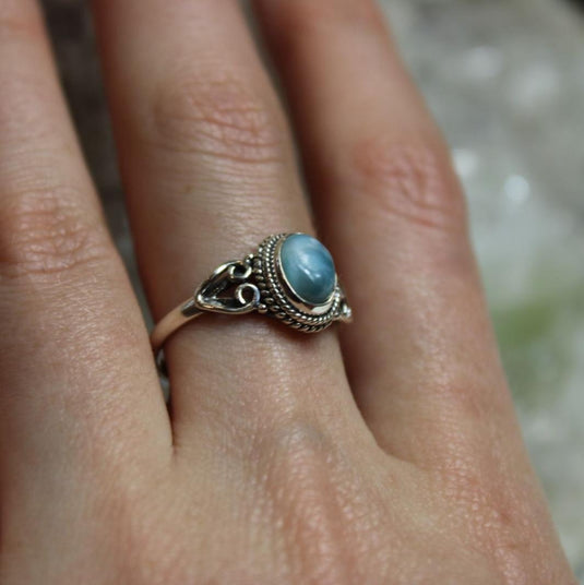 Close-up of a hand wearing a Larimar ring, showcasing the gemstone's unique blue colour against a crystal background.