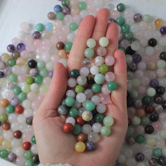 A hand cupping a variety of small, round crystal spheres in various colours and patterns.