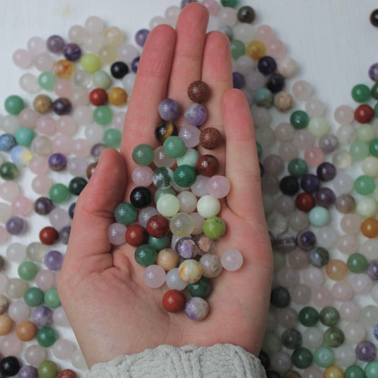 A hand cupping a variety of small, round crystal spheres in various colours and patterns.