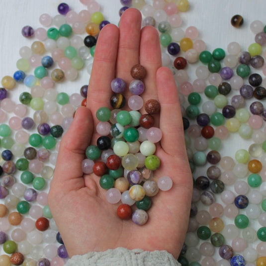 A hand holding a handful of colourful crystal spheres.