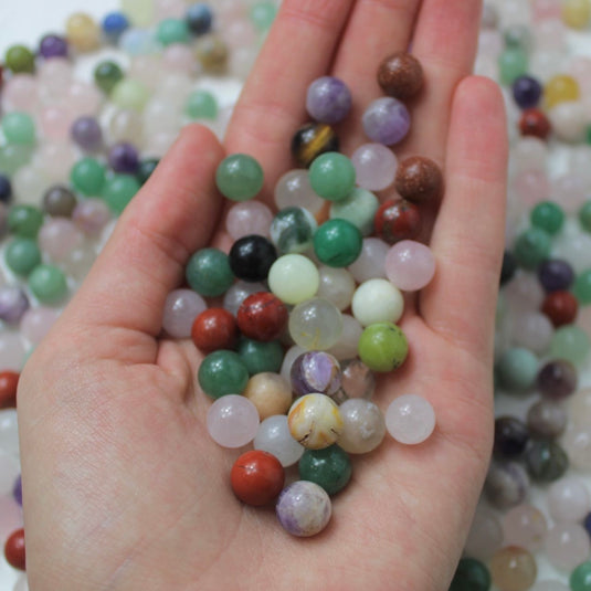 A hand cupping a variety of small, round crystal spheres in various colours and patterns.