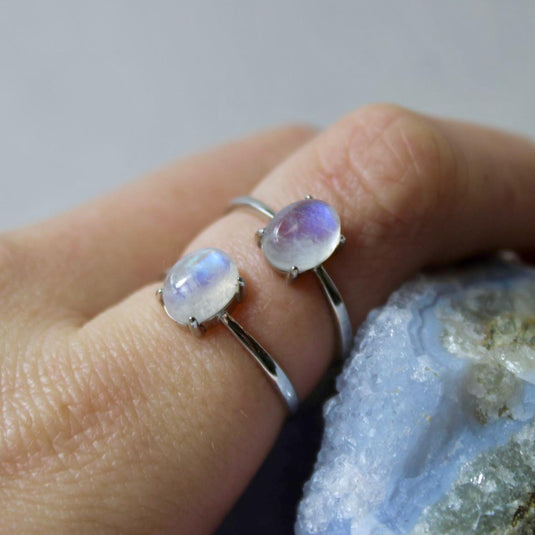 Two silver rings with adjustable bands and a small oval moonstone on a finger.