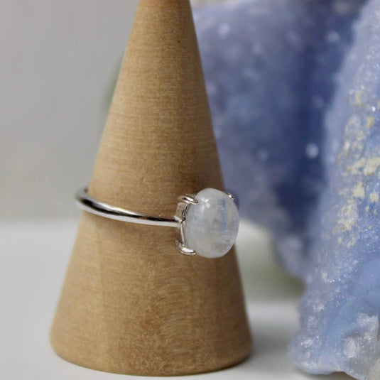 Close-up of a silver ring with an adjustable band and a small oval moonstone on a wooden display.