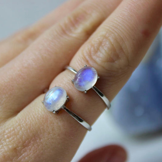 Two silver rings with adjustable bands and a small oval moonstone on a finger.