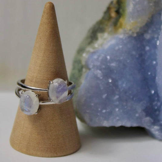 Close-up of a couple of silver rings with an adjustable band and two small oval moonstone on a wooden display.