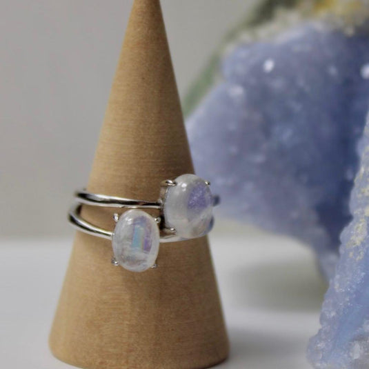 Close-up of a couple of silver rings with an adjustable band and two small oval moonstone on a wooden display.